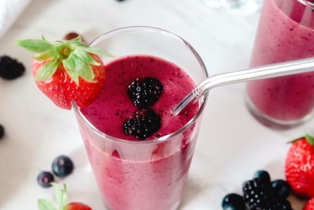 A berry smoothie in a glass topped with berries and a straw