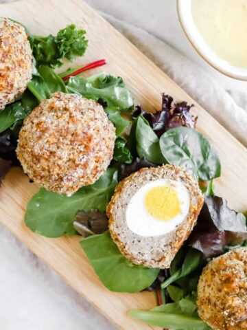 Whole30 Scotch Eggs on a cutting board with greens next to a bowl of mustard sauce