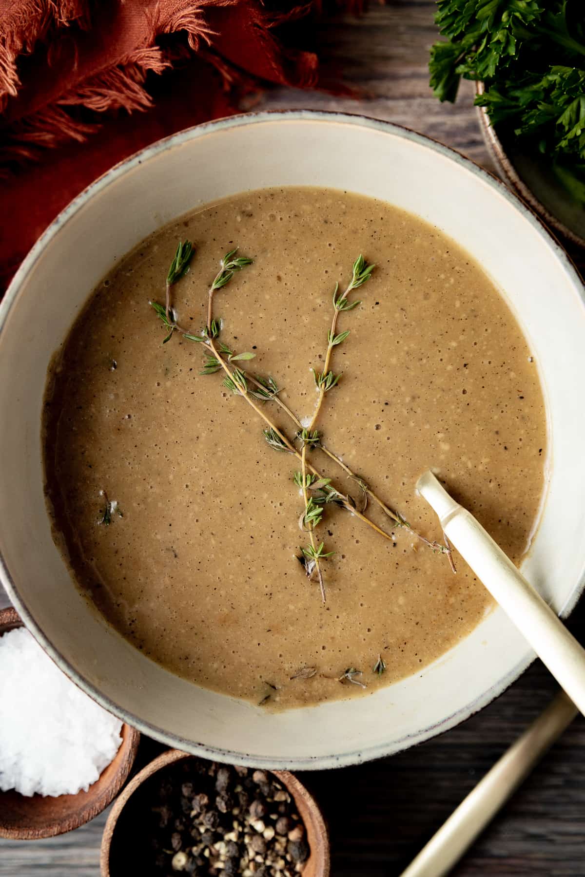 An overhead shot of a bowl of gravy topped with fresh thyme on a wood background.